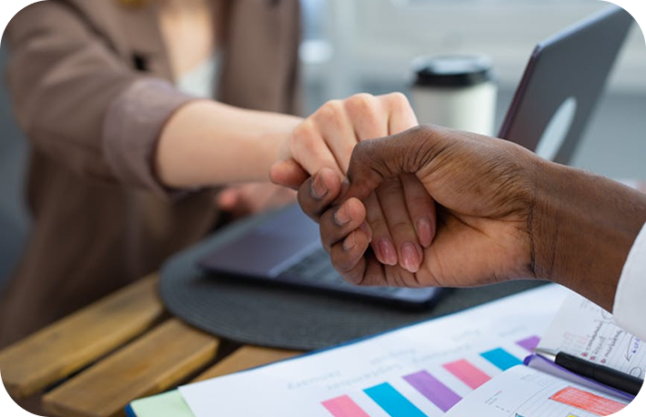 Two people fist bumping over a wooden table with charts and laptop in background